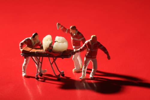 Miniature figures carrying a broken tooth on a stretcher, symbolizing emergency dental rescue or failed treatment repair.