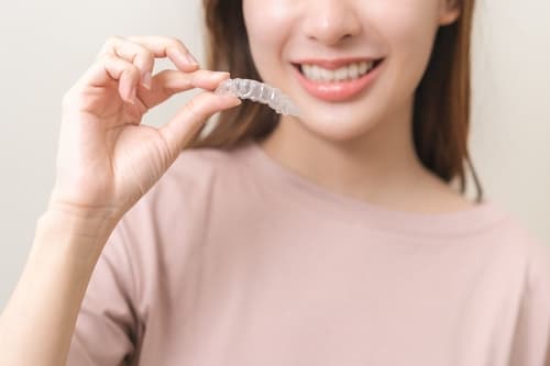 Young Hong Kong woman holding a clear aligner and smiling confidently during her orthodontic treatment.