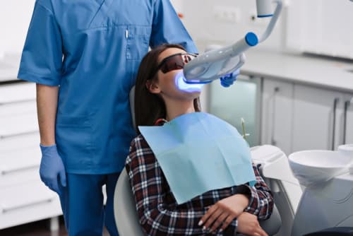 Female patient undergoing blue light teeth whitening at a dental clinic, supervised by a dentist